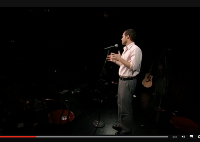 Zrzut ekranu z TED - prelegent w jasnej koszuli, szarych spodniach i czarnych butach